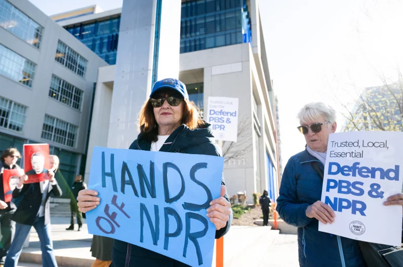 Protestors hold signs supporting funding for NPR